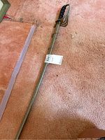 Full view of the metal sword with protective sleeve laying on carpet.