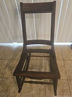 Front angle view of antique wooden rocker frame showing solid base and empty seat frame with carved details on the side supports