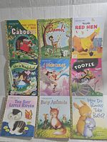 Eighteen assorted Golden Books arranged in two piles showing the colorful illustrated covers of children's books like Bambi, Alice in Wonderland, Hercules, Tootle, and various animal-themed stories.