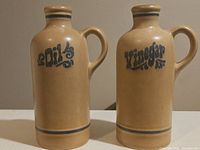 Two tan ceramic bottles labeled 'Oil' and 'Vinegar' with blue decorative text and handles, standing side by side