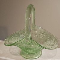 Side view of green translucent glass basket showing detailed floral and scroll embossed Chantilly pattern, the flared edges and handle