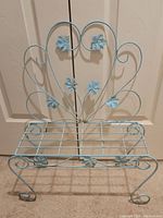 Front view of vintage metal floral plant stand showing scrollwork and flower decorations.