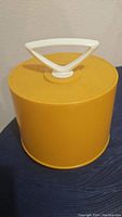Photo of the closed cylindrical yellow plastic Disk-Go-Case with a white handle on top, showing external condition and design.