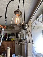 Two Mid-Century Modern ZVO Admite ceiling lights hanging next to each other, showing cage metal design with a lit Edison bulb inside one unit and the other cleared glass bulb.