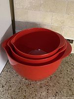 Three red vintage mixing bowls nested inside each other showing size difference and shape.