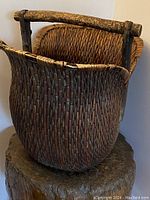 Front-side view of antique primitive Chinese woven basket showing deep rounded bulbous shape, tight elongated weave pattern, and rustic carved wooden handle spanning the top opening.