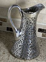Overall view of glass pitcher with silver overlay floral pattern and handle visible