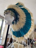 Side view of the war bonnet on mannequin showing teal feathers, white fur, and bead decoration.