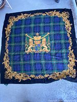 Square wool scarf with blue and green plaid, black border, gold ornate frame and central crest motif.