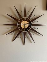 Front view of full sunburst clock showing teak wood rays and metal dial