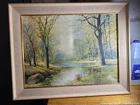 Framed original landscape painting showing autumn or early winter trees by a river with a misty background, artist signature visible on bottom right.