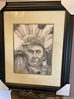 Framed pencil drawing of Indigenous person with eagle headdress, signed Arnold Alex Blacksmith, viewed front facing, showing drawing details, matting, and black frame with corner protectors.