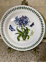 Front image showing 11-inch Portmeirion botanical garden plate with blue agapanthus flowers, three butterflies, and green leaf border.