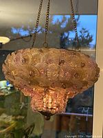 Photo of vintage ornate hanging candle holder chandelier illuminated showing layered translucent glass shells and beads, hanging by chains.