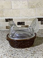 Front side view showing clear glass hen nest cover on brown basket dish on countertop
