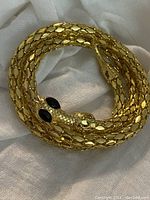 Full view of the coiled gold tone snake bracelet showing its textured scales and overall design.