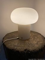 Vintage IKEA Dejsa table lamp with opal glass shade lit on a dark wooden textured surface.