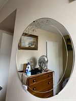 Photo of the full round mirror hanging on the wall over a wooden dresser, showing the etched floral design at the top edge.