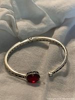Photo of the silver bangle showing the red faceted stone and black bead accents on a light fabric background.
