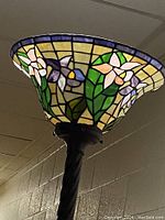 Close-up of stained glass lamp shade showing floral design in green, purple, pink, yellow, and cream colors.