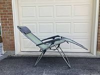 Side view of the green fabric outdoor anti gravity lawn chair fully reclined with footrest extended.