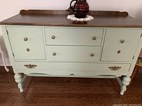 Full front view of the sage green painted buffet with multiple drawers and cabinets on turned legs.