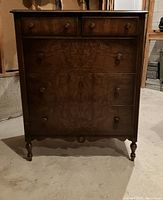 Front view of antique solid wood dresser with five drawers and turned legs.