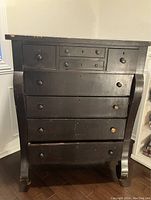 Front view of antique Empire style black painted wooden dresser showing wear and chipped paint.