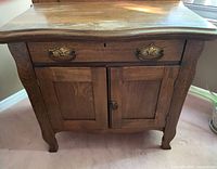 Front view of solid wood antique wash stand showing drawer with brass handles, two cabinet doors with latch, and curved cabriole legs.