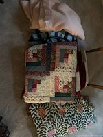 Photo showing five folded blankets stacked including a double quilt style, a floral patterned, a beige blanket, and a blue/black checkered one.