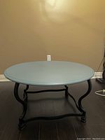 Front and side angle of the blue coffee table showing the curved black metal legs and blue round tabletop