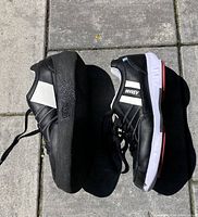 Side view of Asham curling shoes showing black upper with white stripes, brand name, and sole with slider on one shoe.