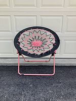 Front view of the round folding lawn chair showing the pink metal frame and woven seat cords.