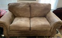 Front view of tan loveseat showing cushions and nailhead trim on rolled arms