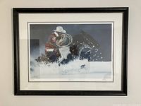 Framed print showing a cowboy on horseback riding through a snowy passage, with visible snow splashes and dynamic composition.