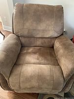 Front view of tan recliner chair showing padded seat, backrest, and armrests with nailhead trim