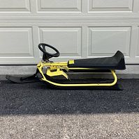 Side view of yellow GT Racer snow sled showing black seat, steering wheel, and front ski