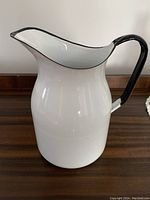 White enamel large jug with black rim and handle shown on wooden surface.