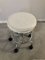 Front angled view of round white cushioned seat on chrome wheeled base showing heavy seat damage.