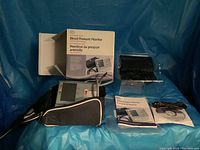 Full lot including device, cuffs, carrying case, instruction manual, and original box with blue backdrop