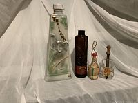 Front view of four collectible bottles including the large embossed Thailand bottle, brown glass bourbon bottle, small Hawaii passion fruit liqueur bottle, and violin-shaped German bottle.