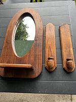 Oval oak framed mirror with two wooden candle holders on a black table outdoors