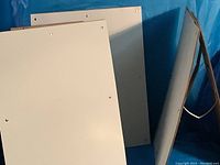 Four plain, lightweight sandwich-type display boards stacked and standing vertically, showing the front surfaces and eyelets for mounting.