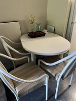White oval table with extra leaf extension and four cushioned chairs around it, placed indoors near wall.