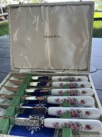 Six Crown Derby steak knives with floral handles neatly arranged in original box with padded satin lining.