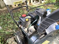 Side view showing engine assembly, handle, part of auger housing with Yard-Man decal and traction tire.
