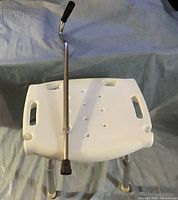 White plastic tub chair seat visible with cutout handles, metal legs, and adjustable metal cane resting on top.