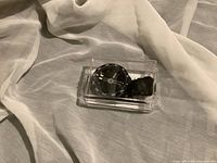 Compass with black strap in transparent plastic case on white fabric