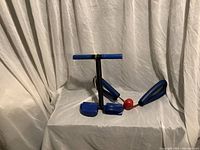 Blue padded fitness gadgets including thigh master and arm workout device on white surface with white backdrop.