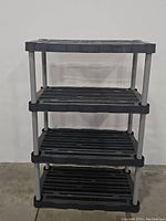 Front full view of 4-tier black plastic shelving unit with metal poles against a white wall.